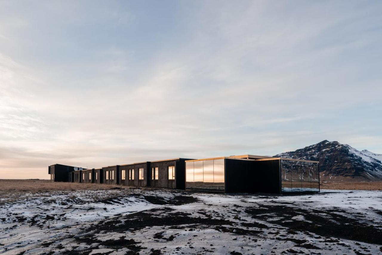 Hotel Umi Iceland black mirrored-glass modular hotel on volcanic plain with snow-capped mountain