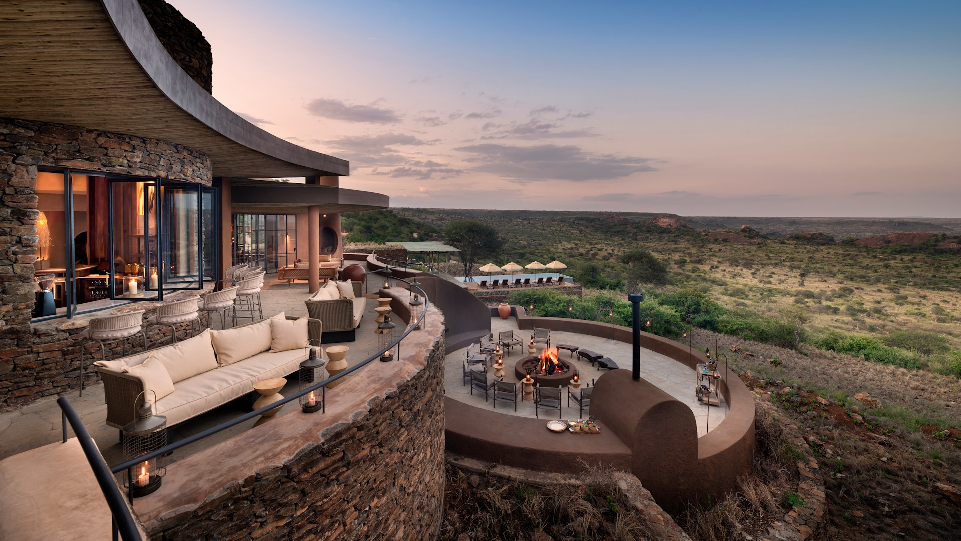 AndBeyond Suyian Lodge Kenya curved stone lodge with outdoor fire pit, sweeping savannah view at dusk